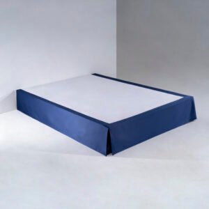 A tailored navy blue hotel bed skirt with clean box-pleated corners draped smoothly over a luxury bed base