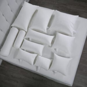 Overhead view of an extensive collection of white hotel pillow inserts in various sizes including rectangular bed pillows, square decorative cushions, and bolster rolls