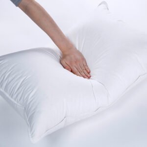 Hand pressing down on a highly resilient, fluffy white hotel collection pillow insert to demonstrate its superior shape recovery and supportive loft