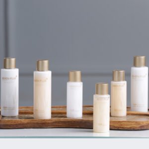 Seven Plus London luxury hotel toiletries with cereal protein ingredients, elegant white and cream bottles with matte gold caps on a wooden tray