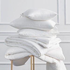 A stack of fluffy white hotel pillow inserts and a thick down-alternative comforter draped over a golden modern frame