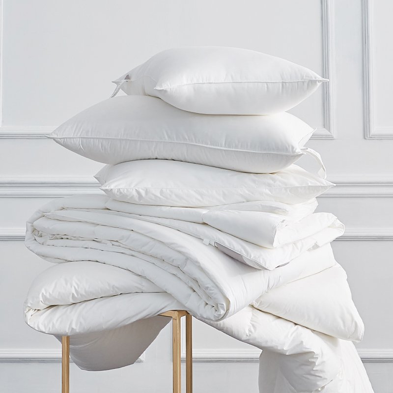A stack of fluffy white hotel pillow inserts and a thick down-alternative comforter draped over a golden modern frame