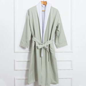 A premium dual-layer luxury hotel bathrobe in sage green with a contrasting white collar lining and matching white piping on hangers