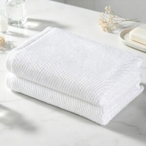 Stacked white waffle weave hotel towels showcasing three-dimensional honeycomb texture on a marble bathroom vanity