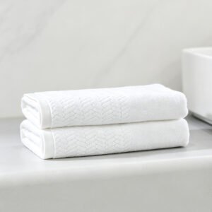Stacked white luxury hotel towels featuring detailed herringbone chevron dobby border weave and woven brand tag