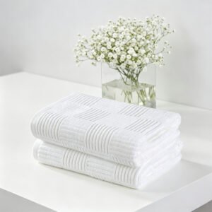 Stacked white checkerboard jacquard hotel towels showcasing three-dimensional block texture next to white flowers on a vanity