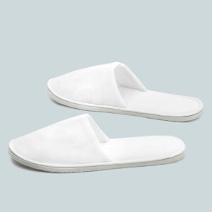 Pair of pure white closed toe velour hotel slippers with flat stitched edges on a soft grey background