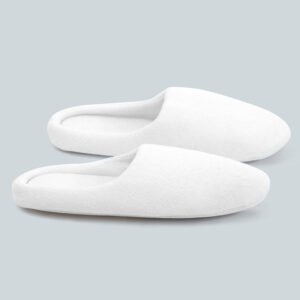 Pair of pure white plush velour closed toe hotel slippers with thick padded edges on a soft grey background