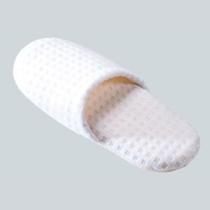 Single pure white waffle weave closed toe hotel slipper resting on a soft grey background