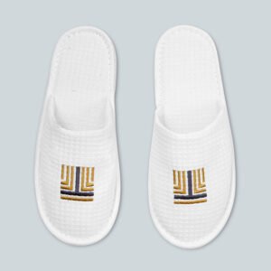 Pair of white waffle weave closed toe hotel slippers with custom gold geometric logo embroidery
