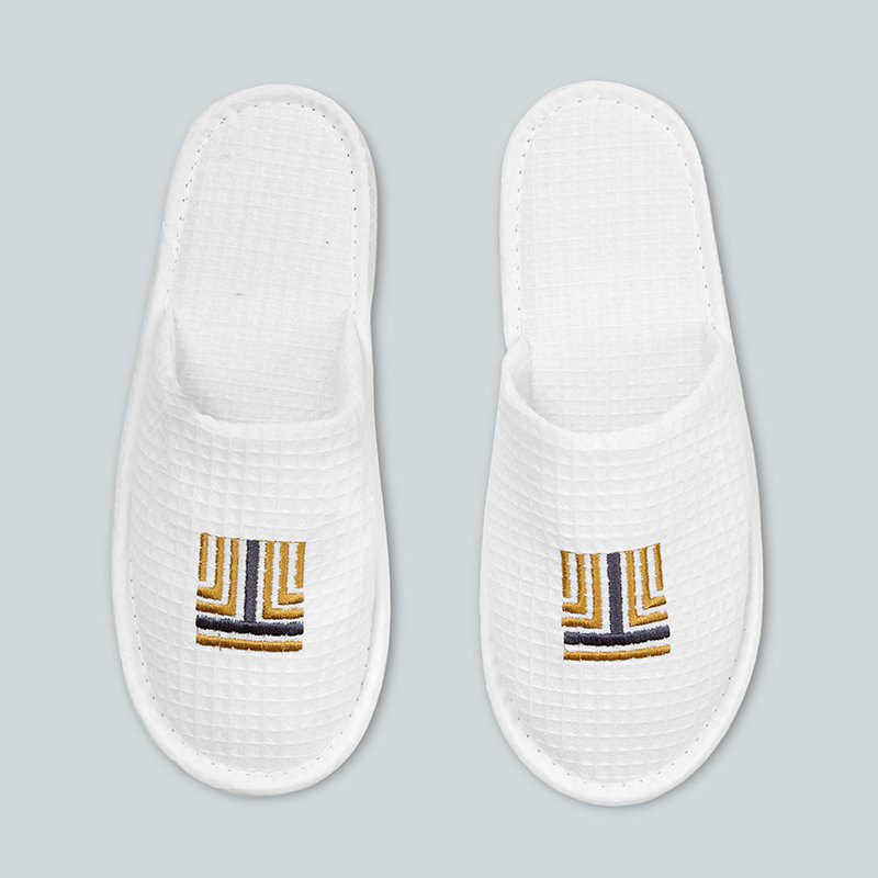 Pair of white waffle weave closed toe hotel slippers with custom gold geometric logo embroidery